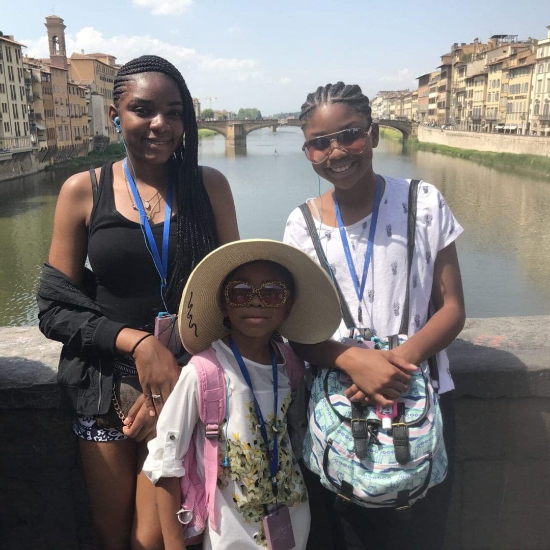 Daughters in Italy Three girls standing on a bridge over water.